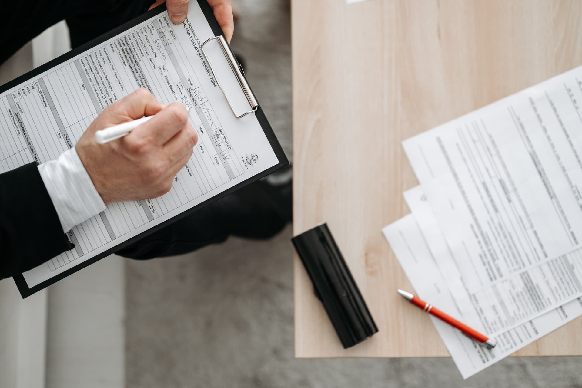 Hands writing notes on a clipboard beside paperwork, illustrating claim documentation