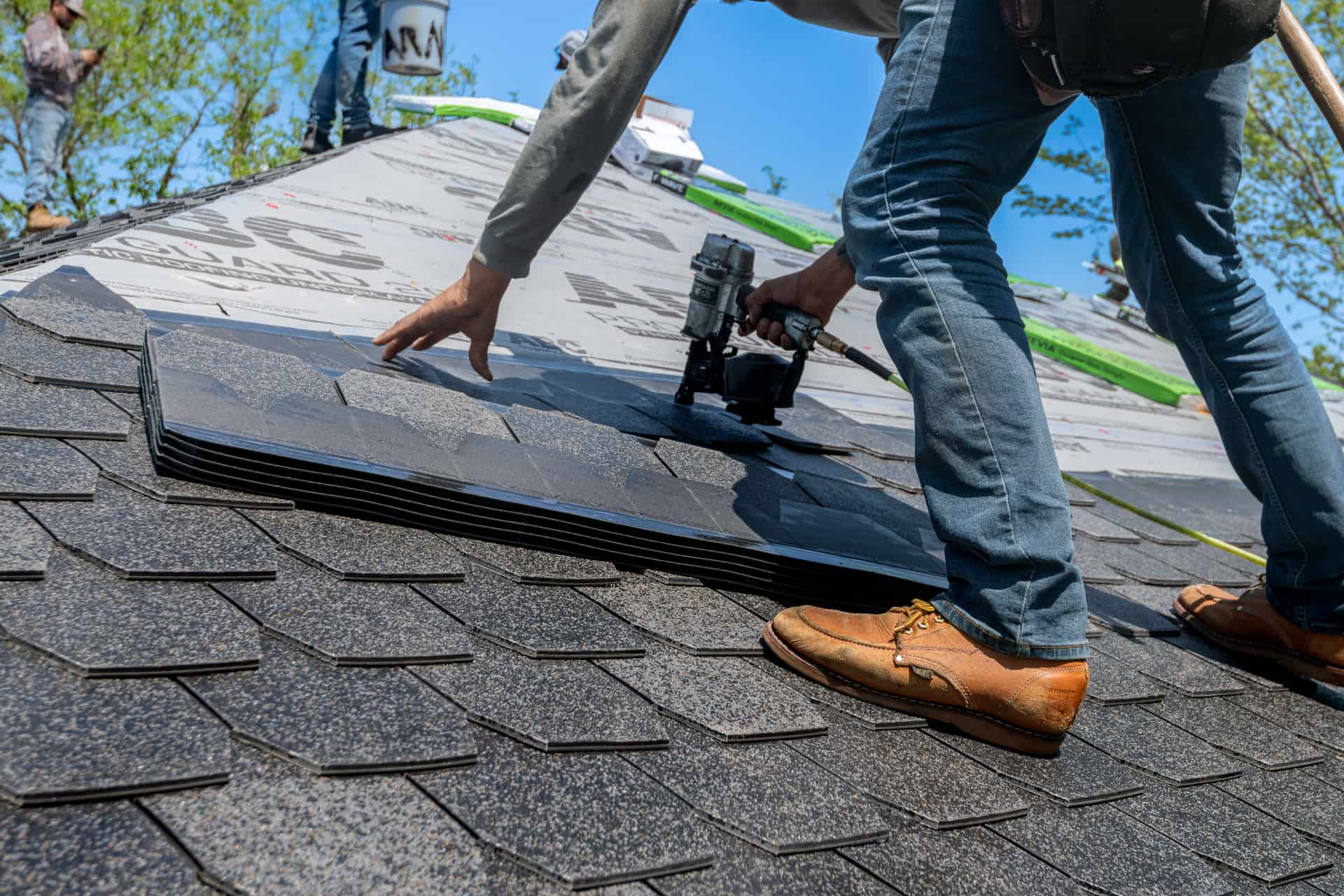 Roofer working across a residential asphalt shingle roof, photographed from roof level