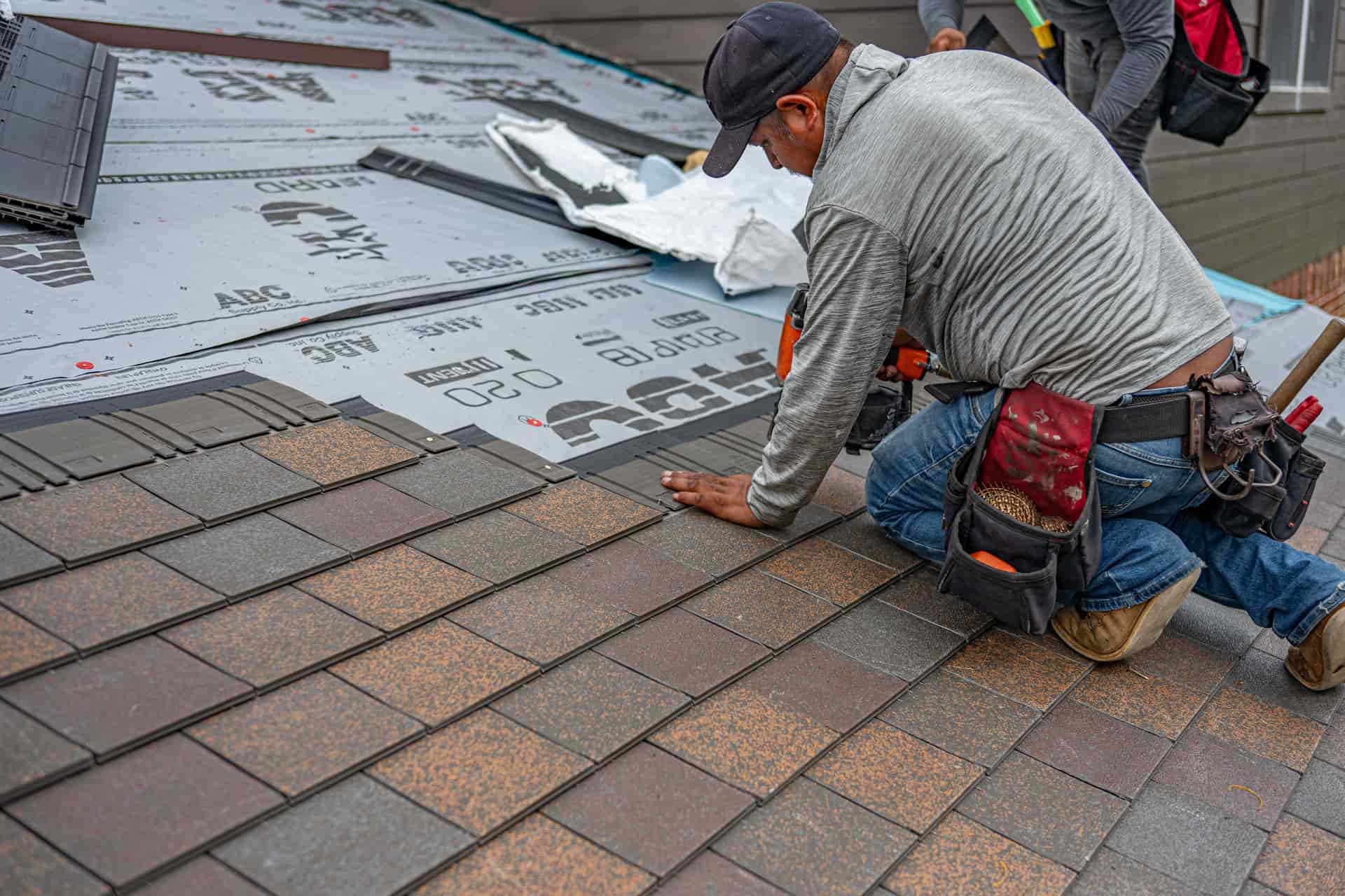 Roofer fastening a course of laminated asphalt shingles over synthetic underlayment